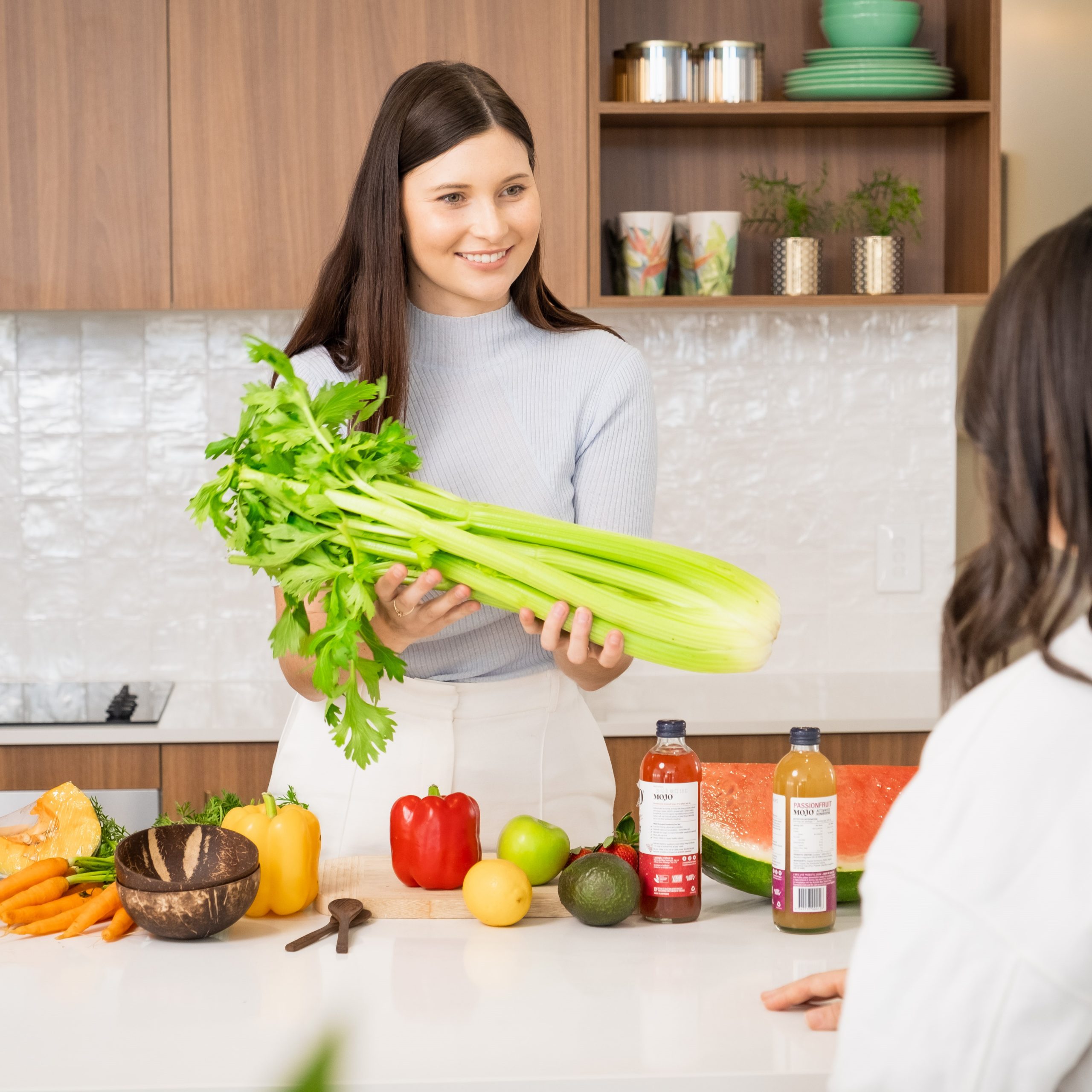 Dietitian standing in a kitchen with mixed fruit and vegetable holding celery