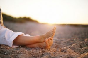closeup image of legs of senior woman sitting relaxed on sandy beach.